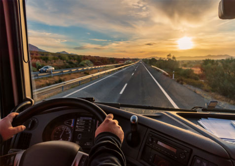 Photo of truck driver riving on highway with sun setting in the background